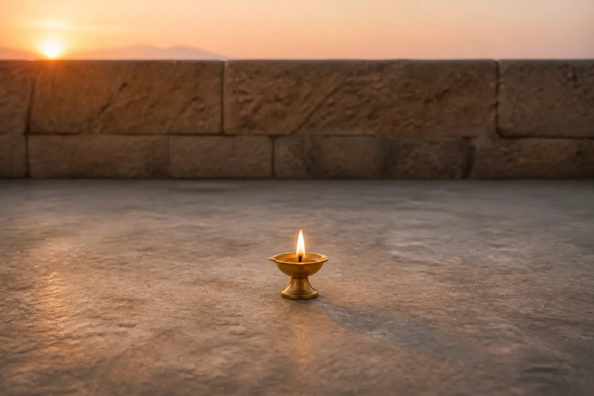 A single lit brass diya centered on a wide, uncluttered stone surface at dawn.